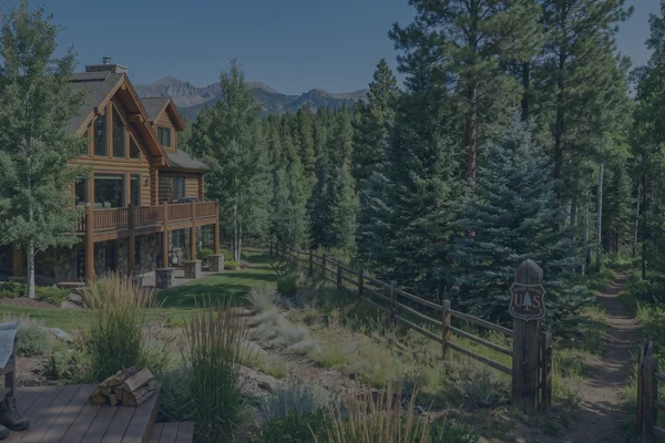 A beautiful luxury mountain home in Pagosa Springs with a backyard that blends seamlessly into the dense pine trees of the San Juan National Forest under a clear blue sky.